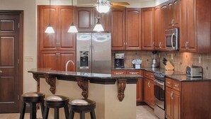A kitchen with wooden cabinets, a central island with stools, stainless steel appliances, and pendant lighting. - 4 Bedroom Presidential Suite inside Disney Property @ Wyndham's Bonnet Creek (Lake Buena Vista)