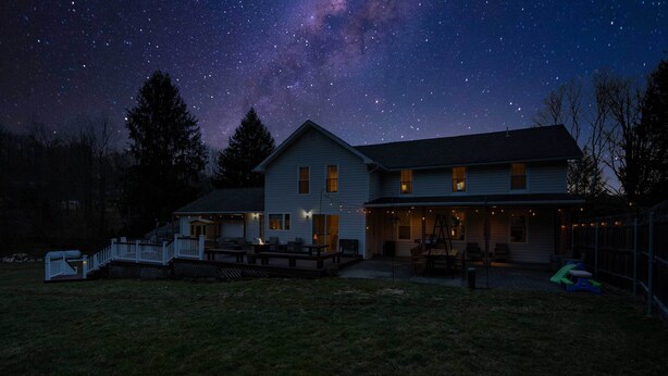 Una casa con terraza, patio cubierto y jardín cercado bajo un cielo estrellado.