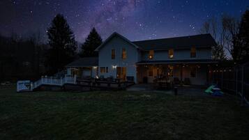 Une maison dotée d’une terrasse, d’un patio couvert et d’une cour clôturée, le tout sous un ciel étoilé.