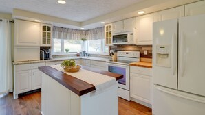 Una cocina con armarios blancos, encimera de madera, microondas integrado, horno y refrigerador.