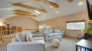 Un salon spacieux avec un plafond haut, des poutres en bois, une grande fenêtre et une cheminée.