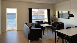 A modern living room with a large window, a sofa, a dining table, and a TV. - Tuukkaq Apartments (Nuuk)