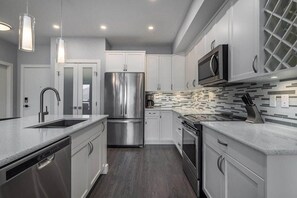 A modern kitchen with stainless steel appliances, white cabinetry, and a tiled backsplash.