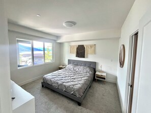 Een slaapkamer met een groot bed, een nachtkastje, een wanddecoratie van macramé en een raam met uitzicht.