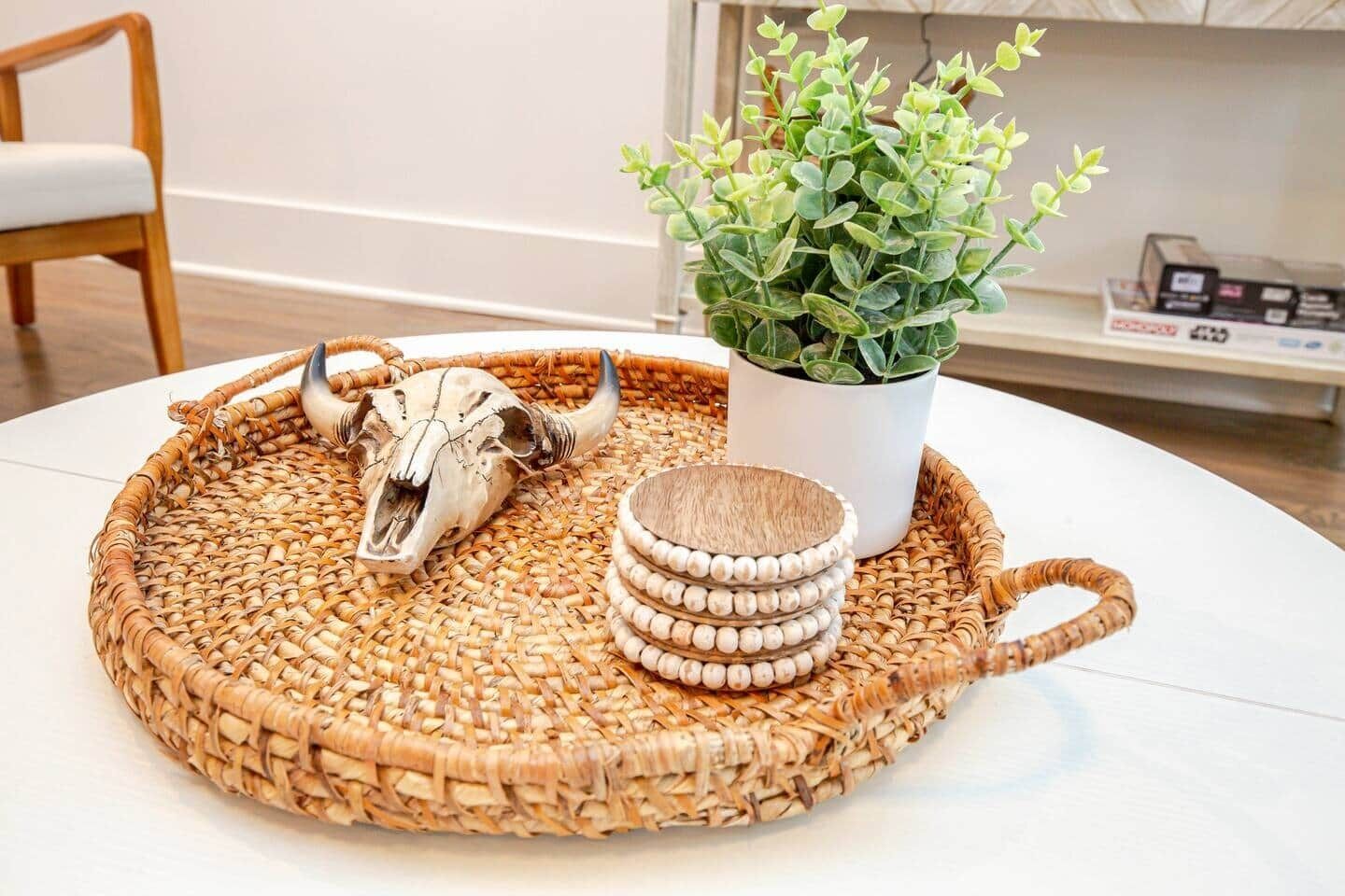 A round woven tray with a skull, a potted plant, and stacked wooden coasters on a white table.