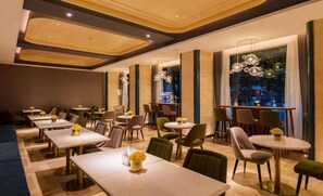 A hotel dining area with multiple tables and chairs, a large window with a view, and modern lighting fixtures. - Yitel Collection (Chengdu DuFU Thatched Cottage & Sichuan Provincial People's Hospital Station) (Chengdu)