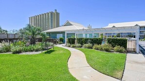 A hotel with a curved pathway, a palm tree, and a tall building in the background. - Beach Bella-Sleeps 8, 3 min Walk to Beach (Destin)