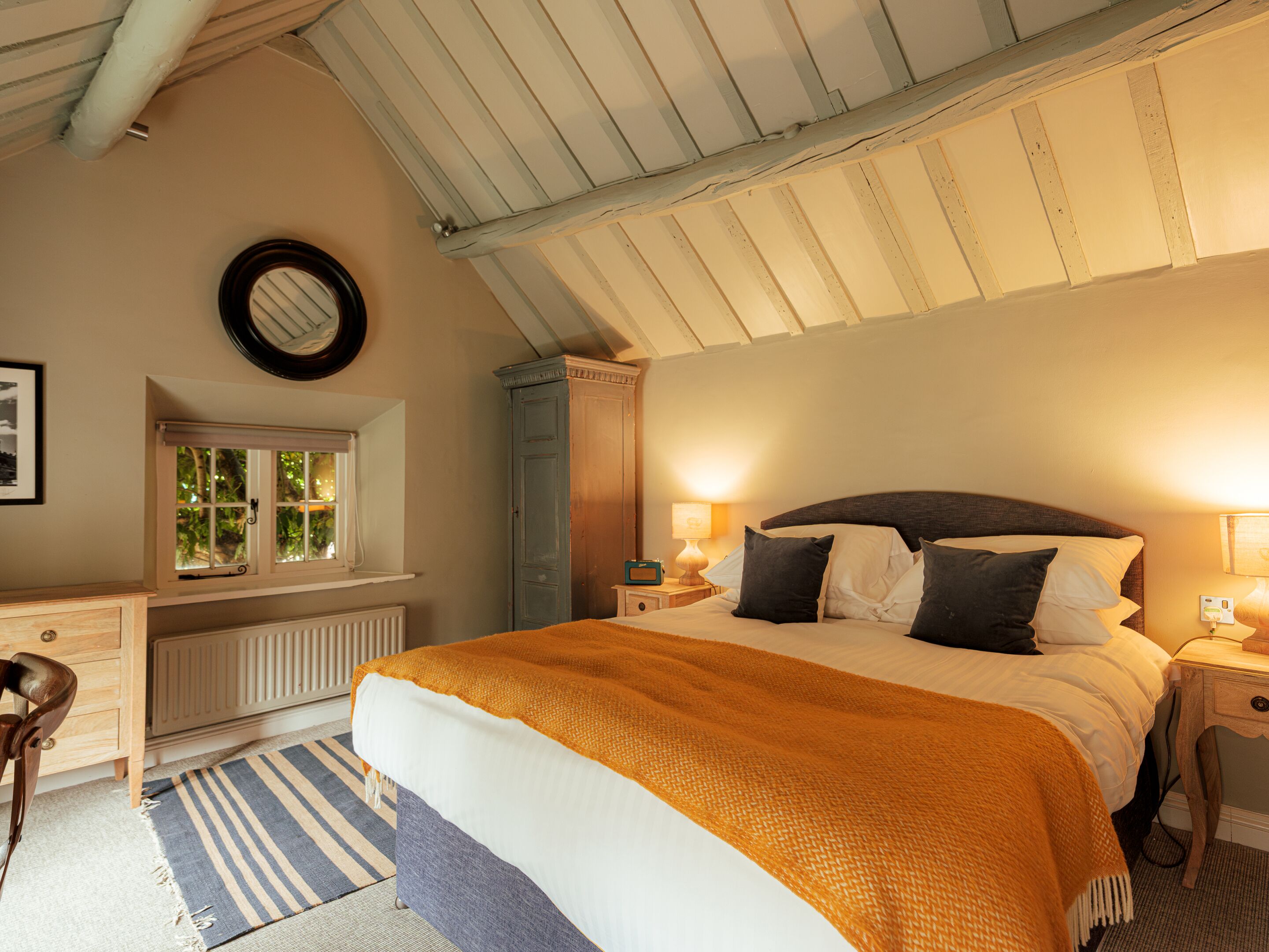 Ein Schlafzimmer mit Bett, Nachttischen, Kommode, Fenster und Heizkörper.