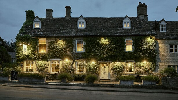 A stone building with ivy-covered walls, multiple windows, and a well-lit entrance. - The New Inn (Cirencester)