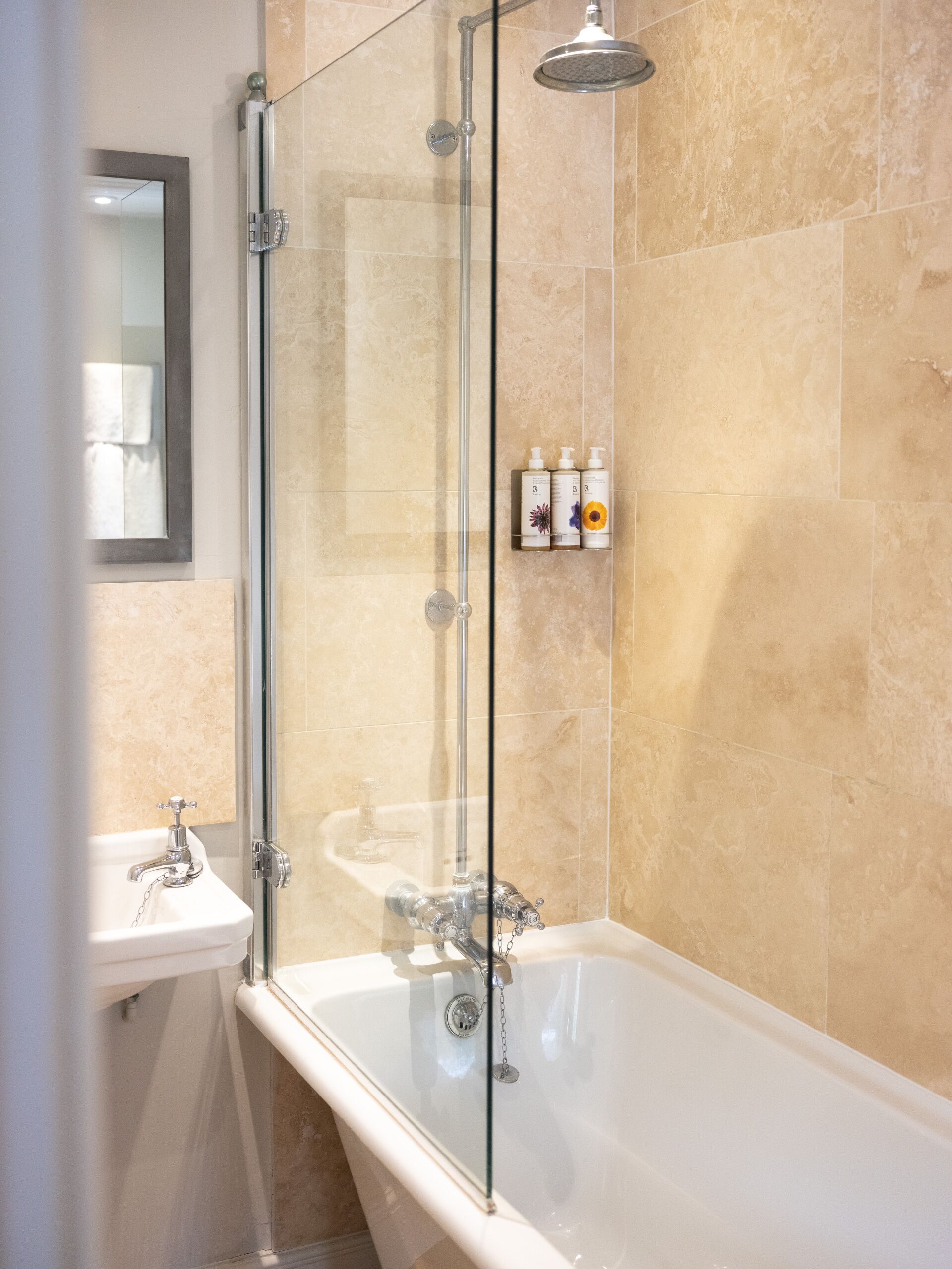 A modern bathroom with a glass-enclosed shower, a standalone bathtub, and a wall-mounted shelf with toiletries.