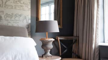 A hotel room with a bed, a lamp, a chair, a mirror, and a window with curtains.