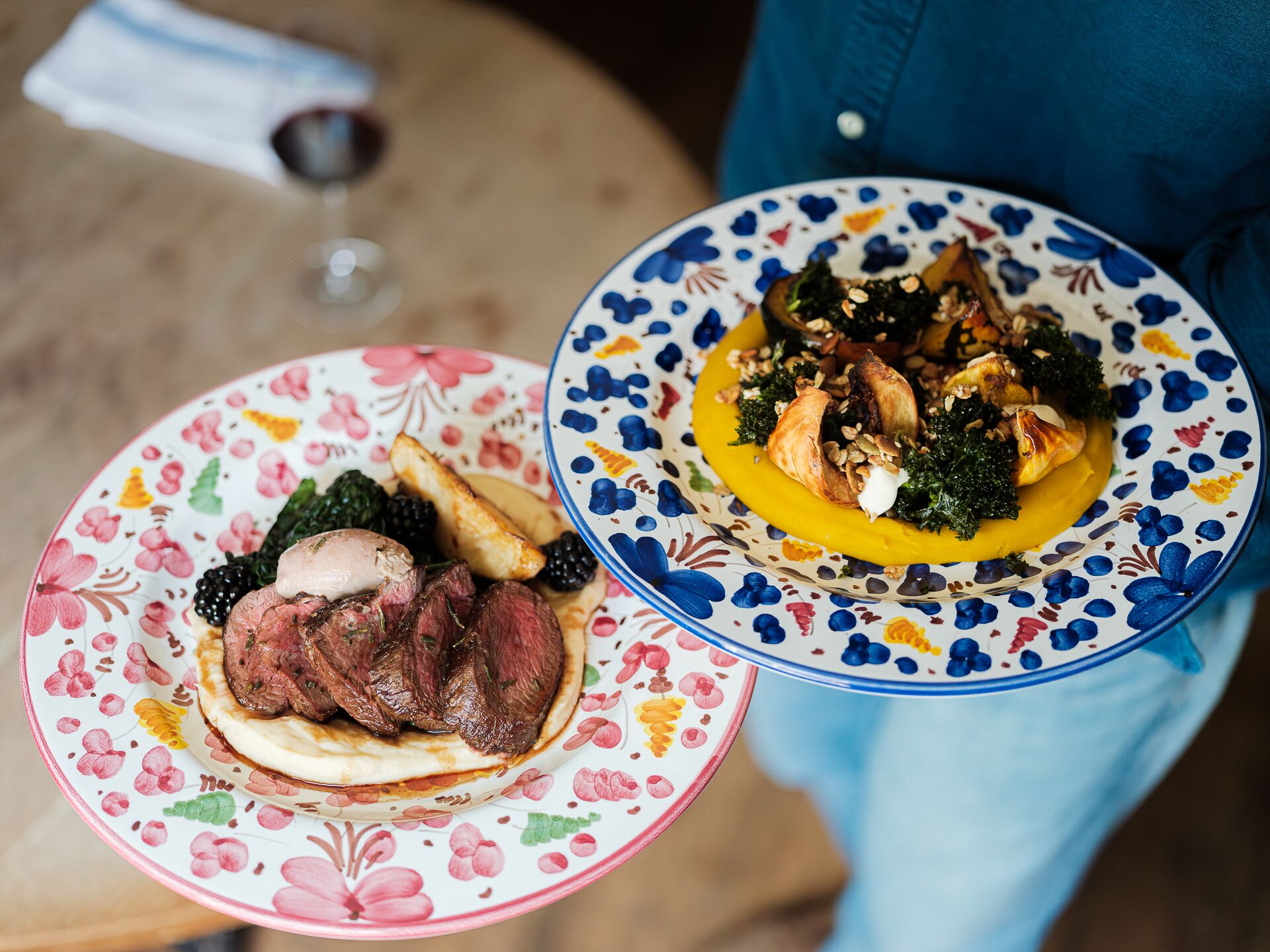 Two plates of food with a glass of wine on a table.