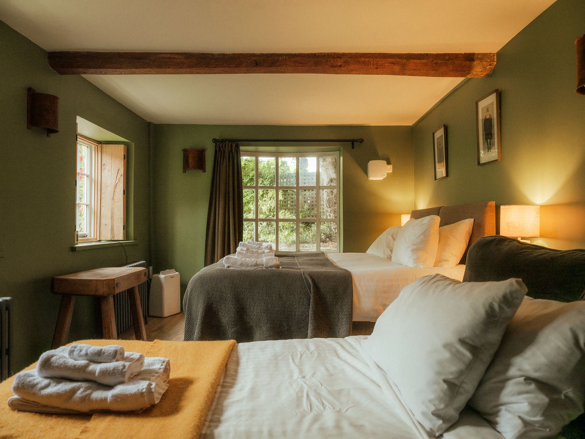 Una habitación con dos camas, una ventana con cortinas, un radiador y una pequeña mesa.