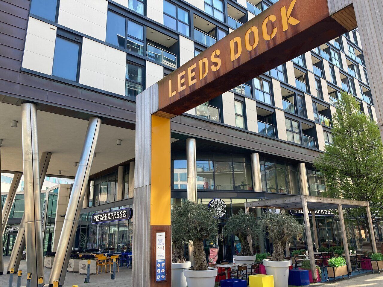 Ein modernes Gebäude mit einem Schild, auf dem "LEEDS DOCK" steht, und einem Pizza Express Restaurant.