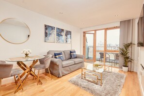 A modern living room with a grey sofa, a round glass table, and a large window with a city view.