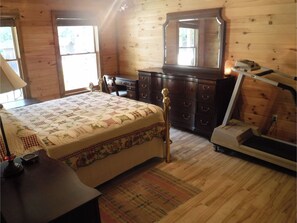 Un dormitorio con cama, cómoda, espejo, máquina de ejercicios y ventana.