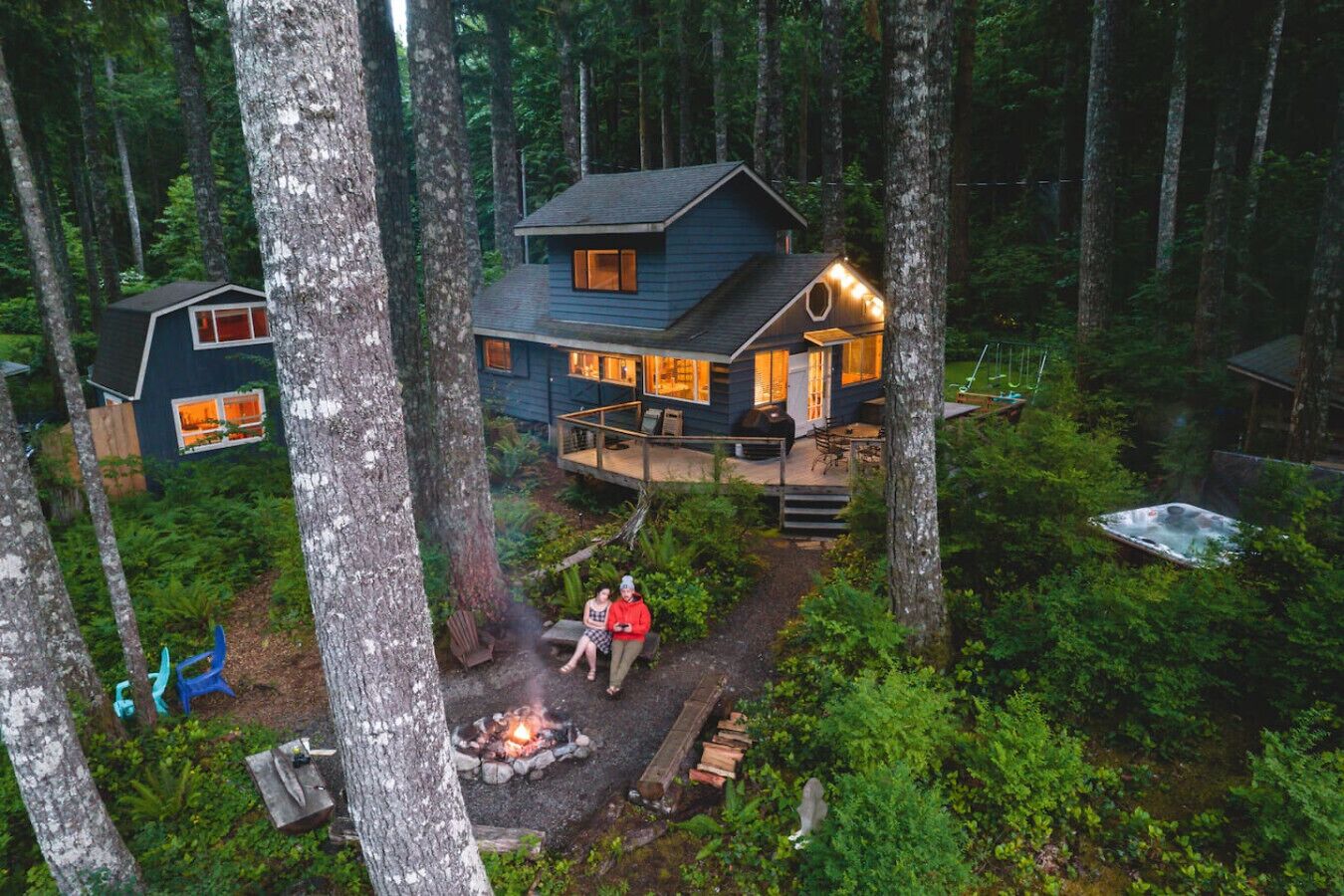 Eine Hütte im Wald mit einer Terrasse, einer Feuerstelle und einem Whirlpool.