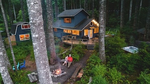 Una cabaña en un bosque con terraza, fogata y jacuzzi.