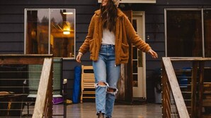 Una persona caminando sobre una cubierta de madera frente a un edificio con un gran ventanal octogonal y luces colgantes.