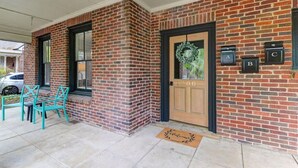 Una casa in mattoni con una porta d'ingresso, un portico con delle sedie e cassette postali etichettate A, B e C.