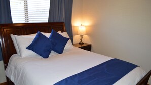 Una cama bien hecha con ropa de cama blanca y azul, un cabecero de madera y una lámpara de noche.