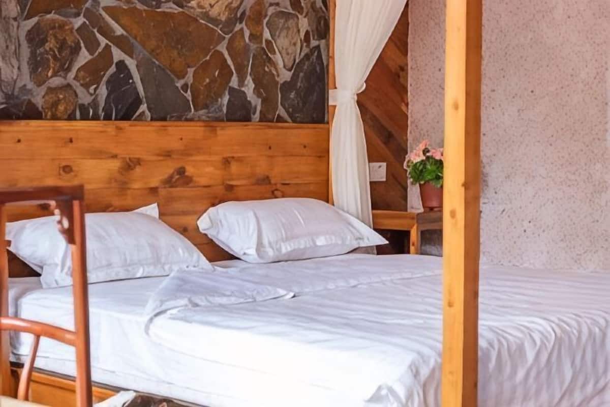 A wooden bed with white bedding, a stone wall, and a small table with a potted plant.