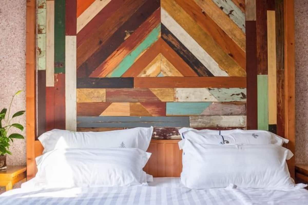 A bed with white bedding, a wooden headboard, and a wall with a geometric wooden pattern.