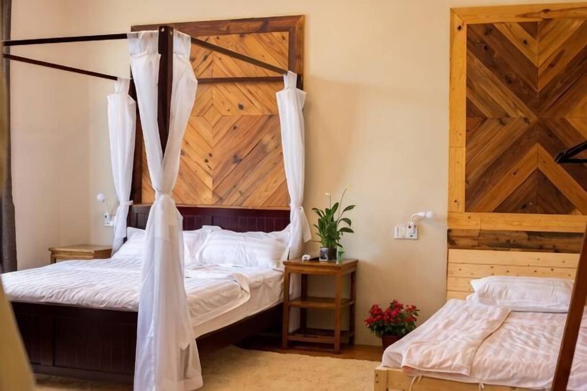 A bedroom with a wooden headboard, a bed with white bedding, a nightstand, and a small table with a plant.