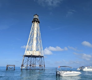 A lighthouse with a metal framework and a white base, surrounded by calm waters and boats. - Bud N' Mary's Fishing Marina (Islamorada)