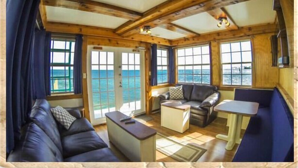 Una habitación con techo de madera, ventanas amplias, un sofá, una mesa y vistas al mar.