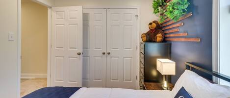 A bedroom with a bed, a nightstand, a lamp, a teddy bear, and a wall-mounted plant.