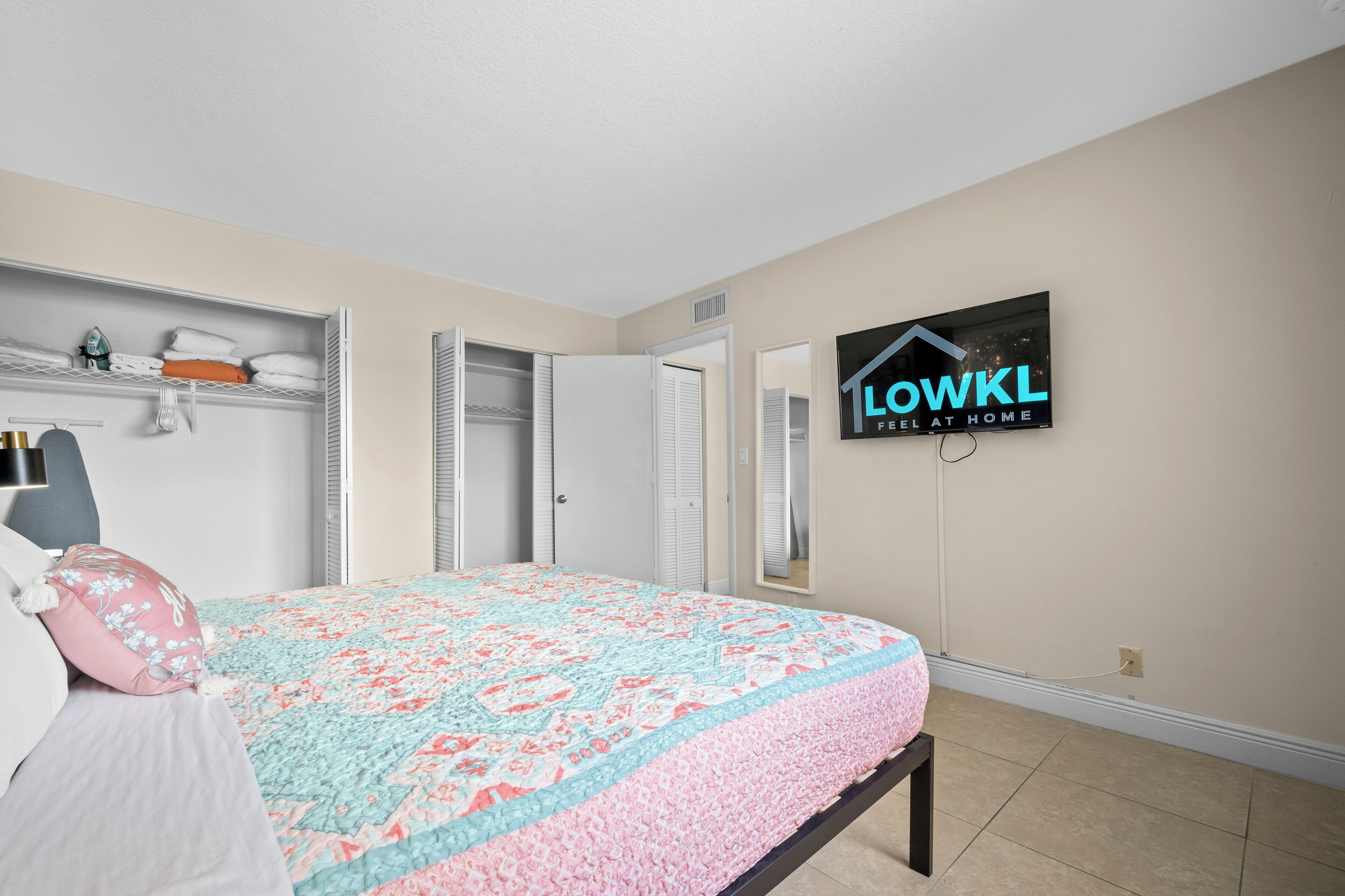 A bedroom with a bed, a TV mounted on the wall, and a closet with sliding doors.