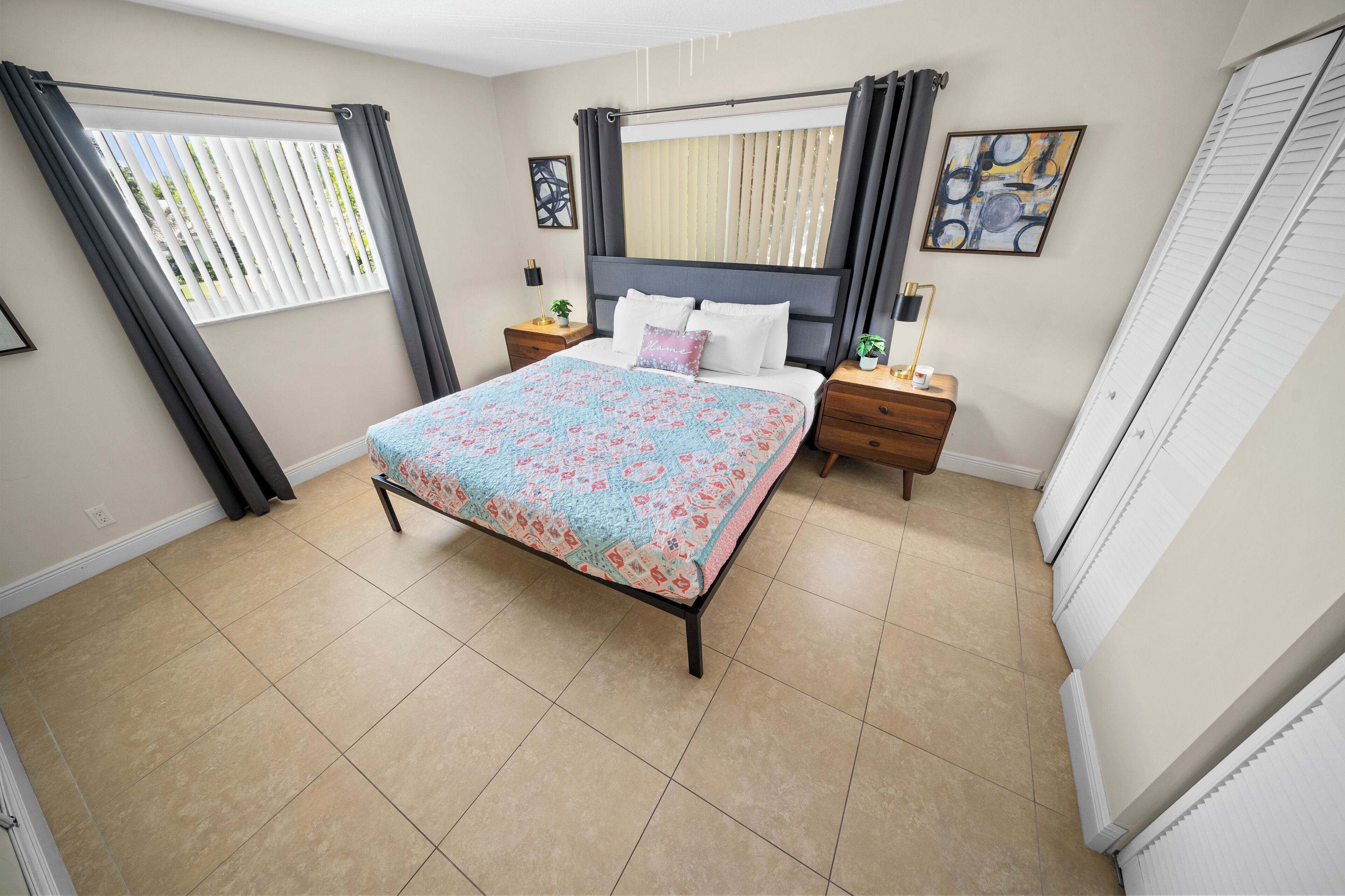 Une chambre à coucher avec un lit, des tables de chevet, une fenêtre avec des rideaux et un tableau accroché au mur.
