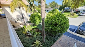 Un barrio residencial con un camino de entrada pavimentado, una barandilla blanca y diversas plantas y árboles verdes.