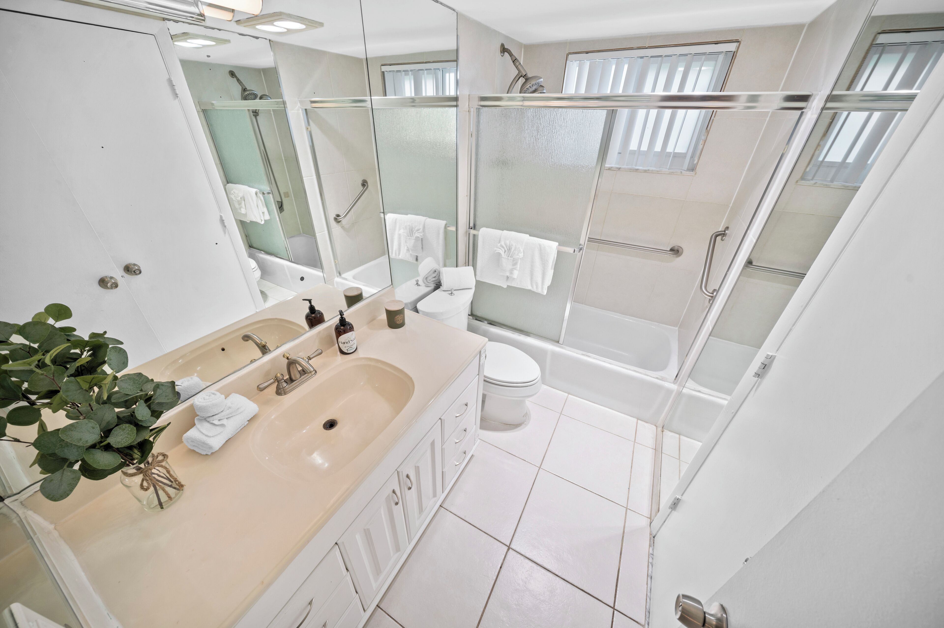 Ein modernes Badezimmer mit einem Doppelwaschbecken, einer Toilette, einer Dusche mit Glastüren und einem großen Spiegel.