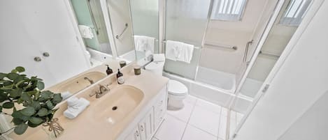 Ein modernes Badezimmer mit einem Doppelwaschbecken, einer Toilette, einer Dusche mit Glastüren und einem großen Spiegel.
