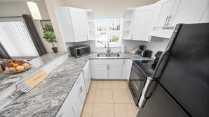 Una cocina moderna con armarios blancos, un refrigerador negro, un microondas y un lavamanos.