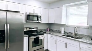 A modern kitchen with white cabinets, stainless steel appliances, and a light wood floor. - Remodeled modern home (Port Richey)