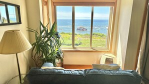Une pièce dotée d’une grande fenêtre donnant sur l’océan, d’un canapé bleu, d’un lampadaire et d’une plante en pot.