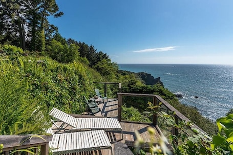 A wooden deck with chairs overlooking a coastal area with rocky outcrops and dense greenery.