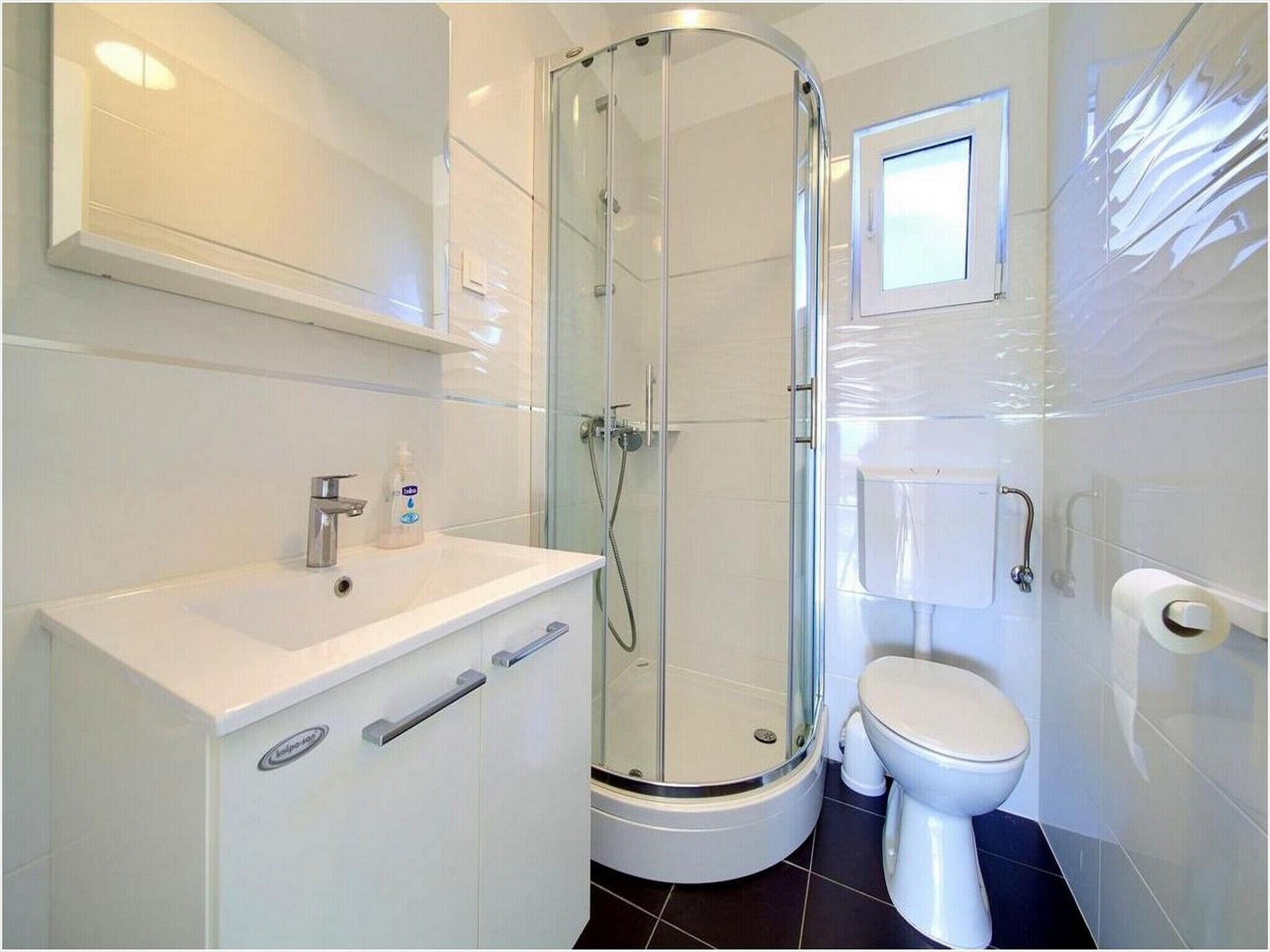 A modern bathroom with a glass-enclosed shower, a white sink with a soap dispenser, and a toilet.