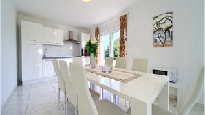 Una cocina moderna con armarios blancos, una campana extractora de acero inoxidable y un comedor con mesa y sillas blancas.
