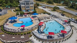 Een resort met twee zwembaden, een speelplaats en een groot gebouw met een stenen gevel.