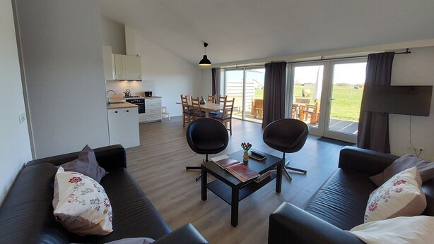 Een moderne woonkamer met een zithoek, een eettafel met stoelen en een keuken op de achtergrond.