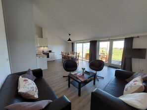 A modern living room with a sofa set, a dining table with chairs, and a kitchen area in the background.