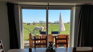 Een eetgedeelte met een tafel en stoelen, een bloemenvaas en uitzicht op een weide met paarden.