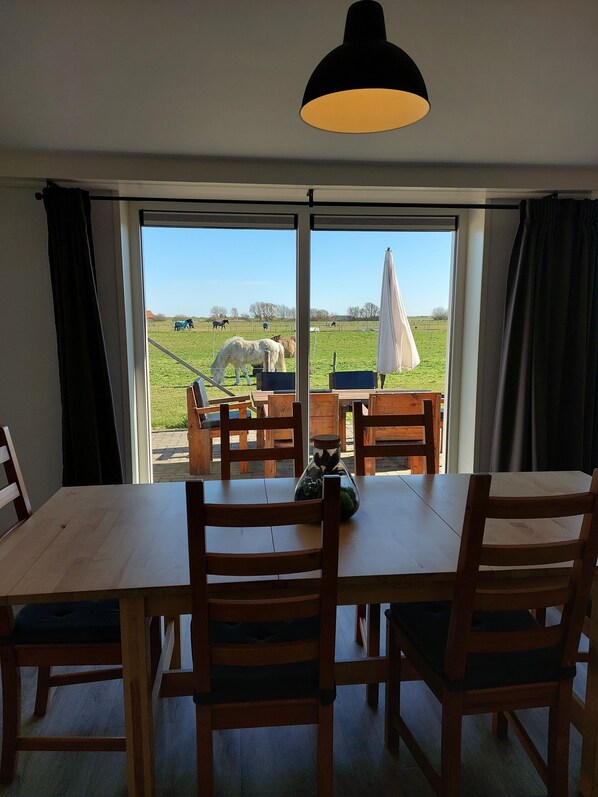 A dining area with a table and chairs, a bottle of flowers, and a view of a field with horses.