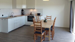 Een moderne keuken met witte kasten, een houten eettafel en een zwart hanglamp.