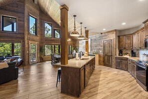 A spacious kitchen with wooden cabinetry, a large island, and a dining area with a view of the outdoors. - Lake Front, Hot Tub, Boat Slip & Next to SDC! (Branson)