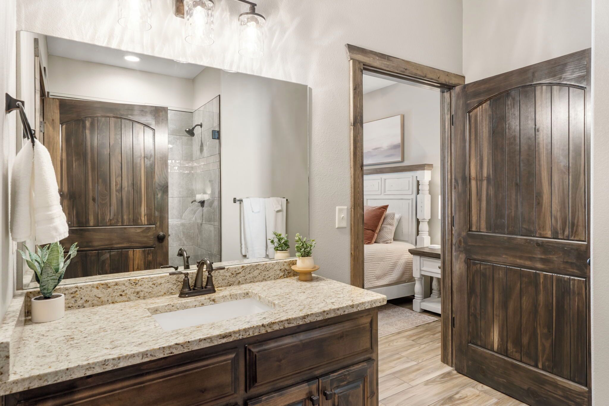 Un bagno con una porta in legno, un lavandino con piano in granito e uno specchio sopra il lavandino.